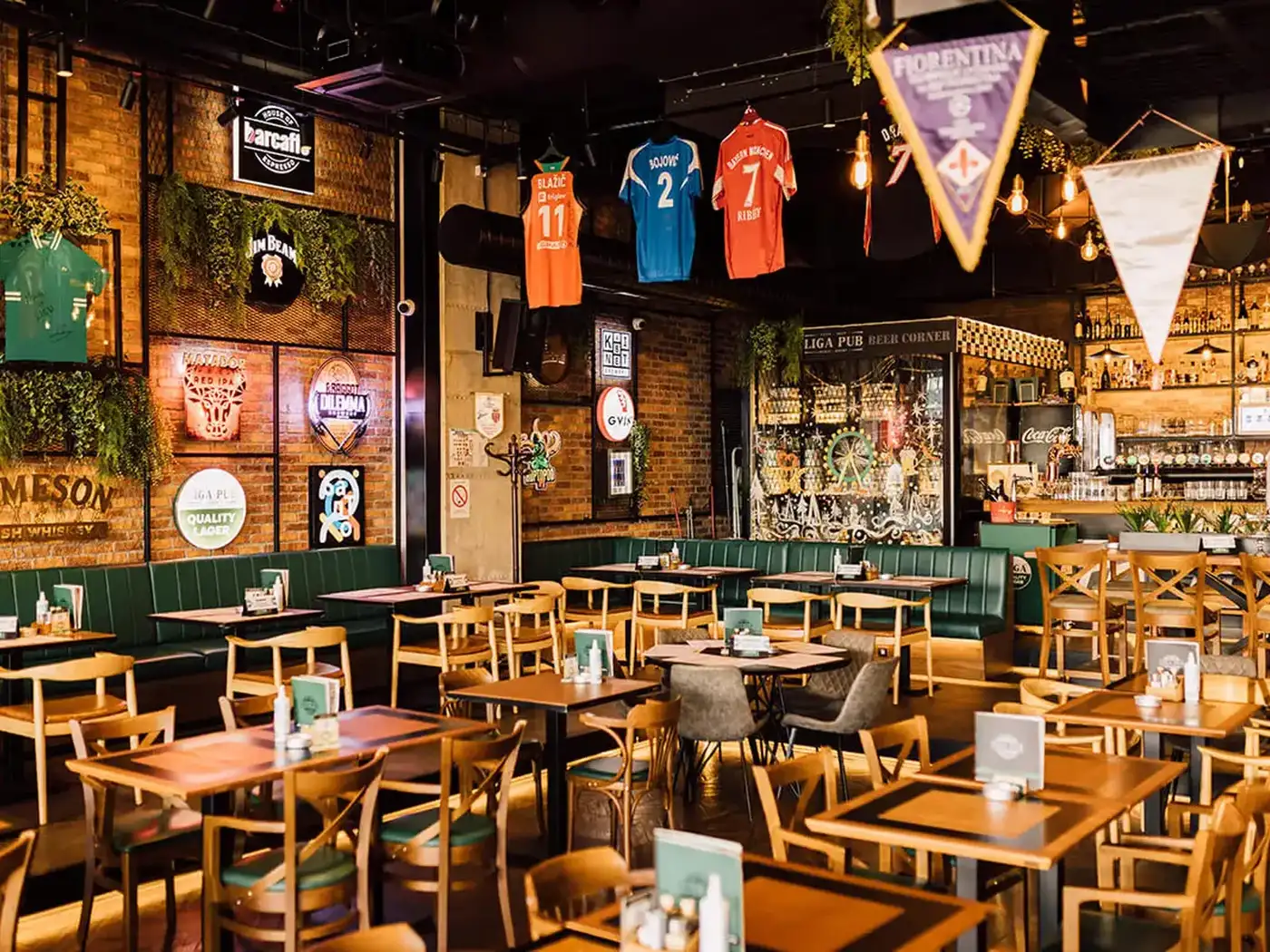 A pub room with woven pendant lights, olive trees in planters and wooden chairs with upholstered seats