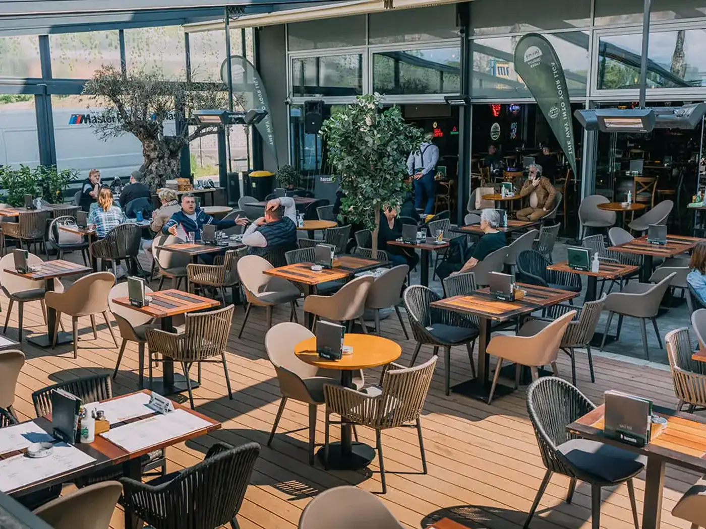 The Liga Pub summer garden with wooden tables and woven armchairs, full of guests