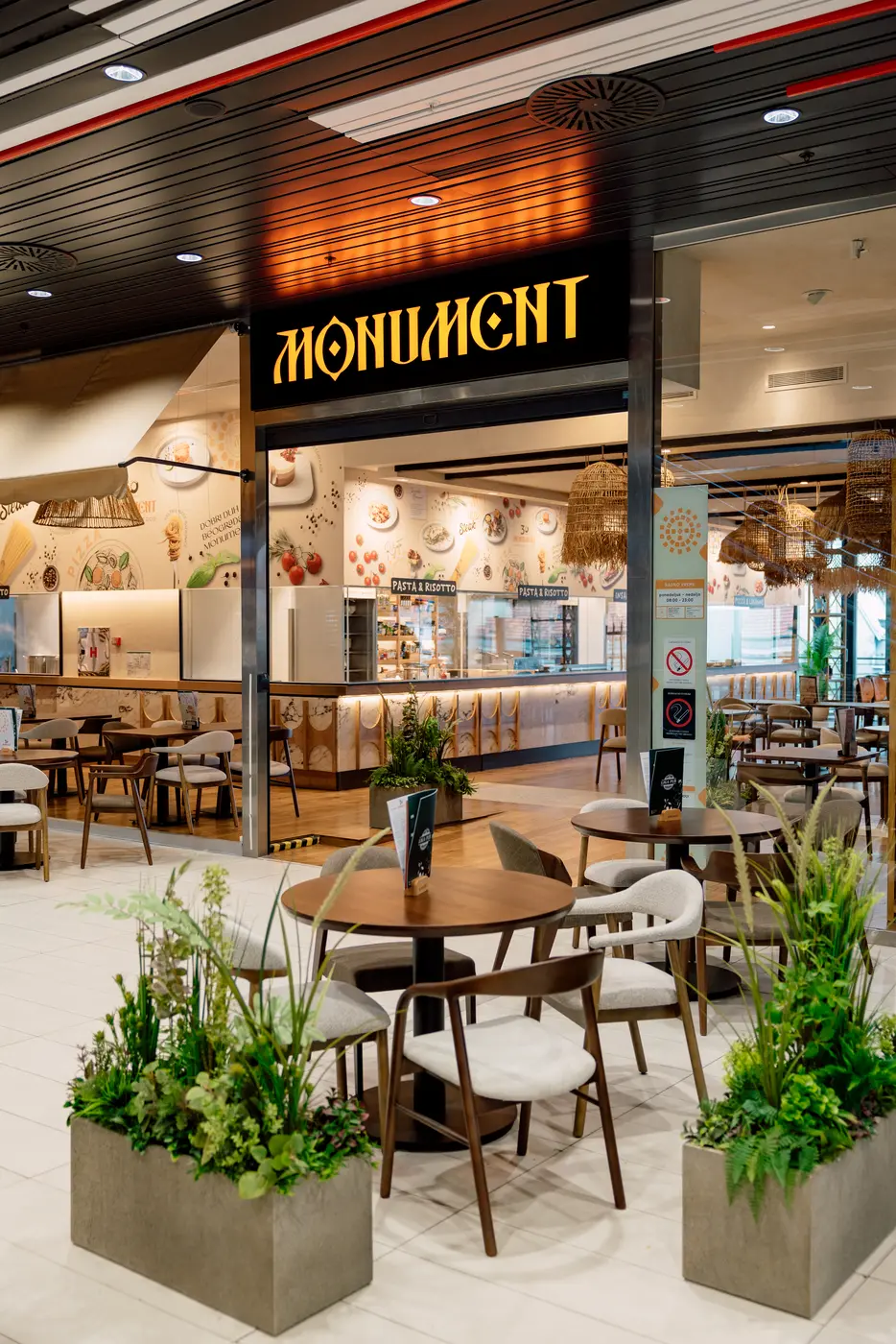 Entrance of Monument restaurant in Rajićeva shopping centre — round tables and upholstered chairs between planters