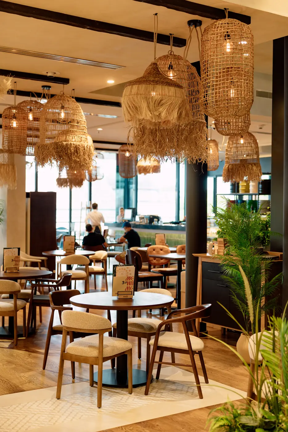 Monument Rajićeva restaurant — round wooden table and upholstered chairs under woven pendant lamps