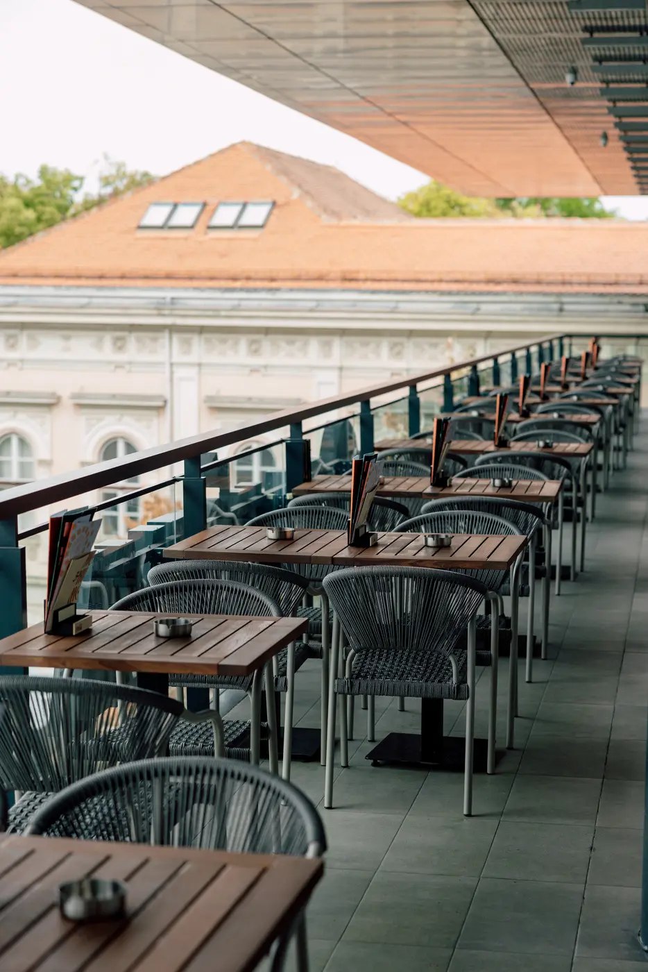 Terrace of Monument Rajićeva restaurant — wooden tables and woven rope chairs
